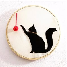 a black cat with a red ball in its mouth on a white wall hanging ornament