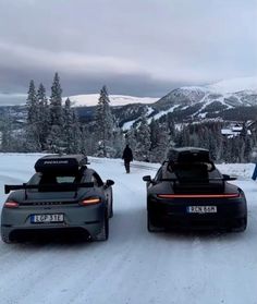 two sports cars parked in the snow with people walking by on skis behind them