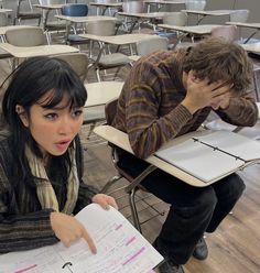 two people sitting at desks with papers in front of them and one person holding a pen