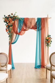 an orange and blue drape with flowers on it next to two chairs in front of a white wall