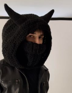 a man wearing a knitted cat mask and black leather jacket is standing in front of a white wall