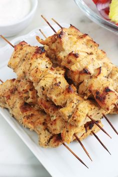 several skewers of food on a white plate next to a bowl of salad