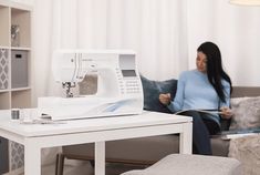 a woman sitting on a couch next to a table with a sewing machine on it