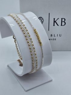 three rows of bracelets with gold beads on white display stand in front of box