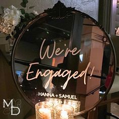 we're engaged sign in front of a round mirror with candles on the table