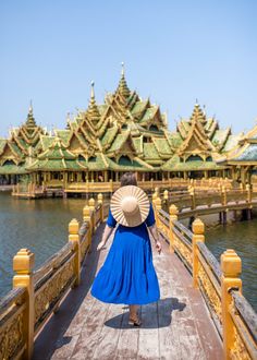 a woman in a blue dress is walking across a bridge with a large hat on her head