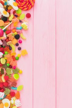 colorful candies and lollipops are scattered on a pink wooden background with copy space