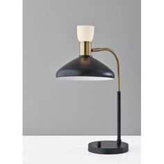 a black and gold desk lamp with a white light on the top, in front of a gray wall