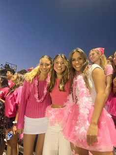 three girls dressed in pink and white posing for the camera at a sporting event with other people behind them