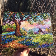 a person holding up a painting in front of a tree and house on the other side