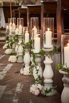 rows of candles lined up on the floor in front of an alter with flowers and greenery