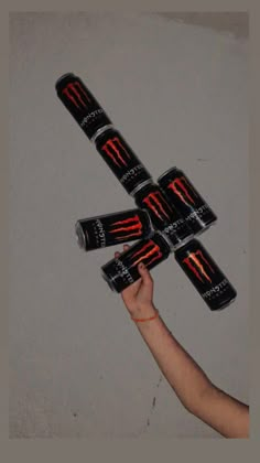 a person holding six cans of energy drink in the air with their fingers on them