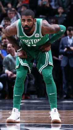 a man standing on top of a basketball court with his hands in the air while wearing green