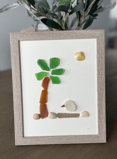 a shadow frame with sea glass and rocks in the shape of a palm tree on a table