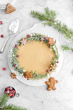 a christmas cake decorated with ginger cookies and greenery on a white platter surrounded by silverware