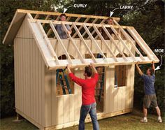 two men are building a small house with windows and sidings on the roof, while another man is standing in front of it