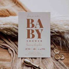 a white card with brown lettering that says ba by shower on it next to some gold buttons