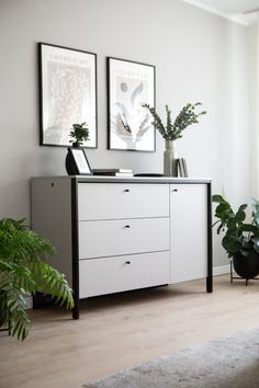 a white dresser with plants and pictures on the wall