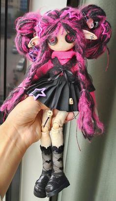 a hand holding a doll with pink hair and black clothes on it's head