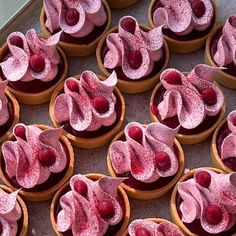 many cupcakes with pink frosting and cherries on them are arranged in rows