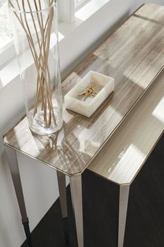 a wooden table with a glass vase and ring holder on it next to a window