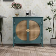 a blue cabinet with wicker doors in front of a wallpapered wall and potted plants