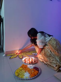 a woman kneeling down next to a plate full of flowers and candles on the floor