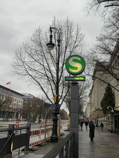 a street sign on a pole next to a lamp post with a green and white letter