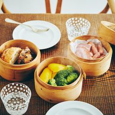 three wooden bowls filled with food on top of a table next to plates and glasses