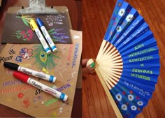 a hand holding a blue fan with writing on it and some crayons next to it