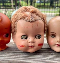 three old dolls are sitting next to each other on a wooden table with one doll's face painted red