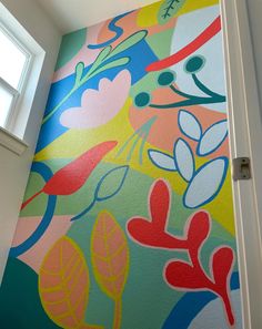 an open door leading to a brightly colored wall with flowers and leaves painted on it