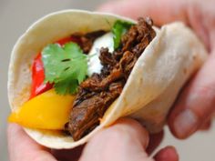 a hand holding a taco with meat, peppers and sour cream on it's side