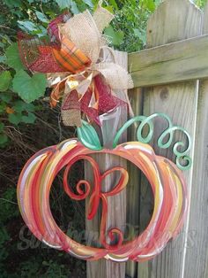 a wooden fence with a metal pumpkin and monogrammed ribbon hanging from it's side