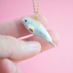 a person holding a tiny white dolphin necklace on a pink background with a gold chain