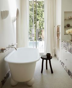 a large white bath tub sitting in a bathroom next to a window with curtains on it