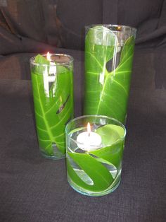 three candles with green leaves in them on a table