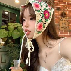 a woman wearing a hat drinking from a straw in front of a brick wall with flowers on it