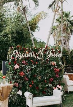 an outdoor seating area with flowers and greenery on the wall, surrounded by palm trees