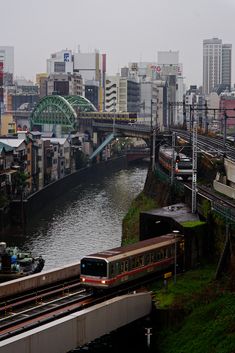 a train traveling over a bridge next to a river in a city with tall buildings