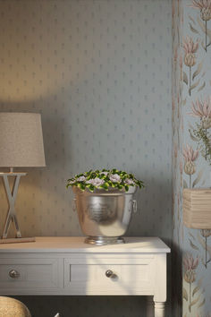 a flower pot sitting on top of a white table next to a lamp and dresser