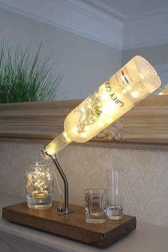 a lighted bottle sitting on top of a wooden table next to glasses and a vase