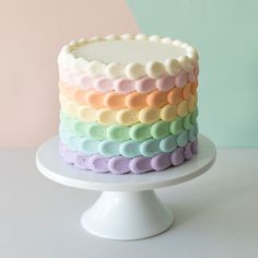 a multicolored cake sitting on top of a white plate next to a pink wall