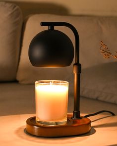 a lit candle sitting on top of a table next to a black lamp and a white couch