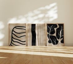 three black and white abstract paintings on wood flooring in an empty room with sunlight coming through the window