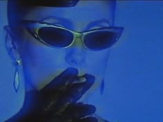 a woman wearing sunglasses and holding her finger up to her mouth in front of a blue background