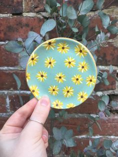 a hand holding a plate with yellow daisies on it in front of a brick wall