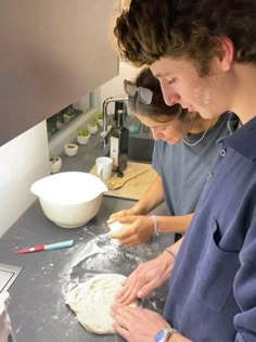 two people in the kitchen preparing food on a counter top and one person is using a knife to cut out dough