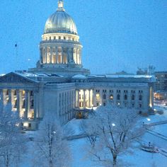 the capital building is lit up at night with snow on the ground and trees in front