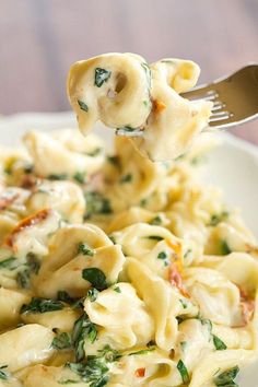 a fork full of pasta with spinach and cheese on it is being held up